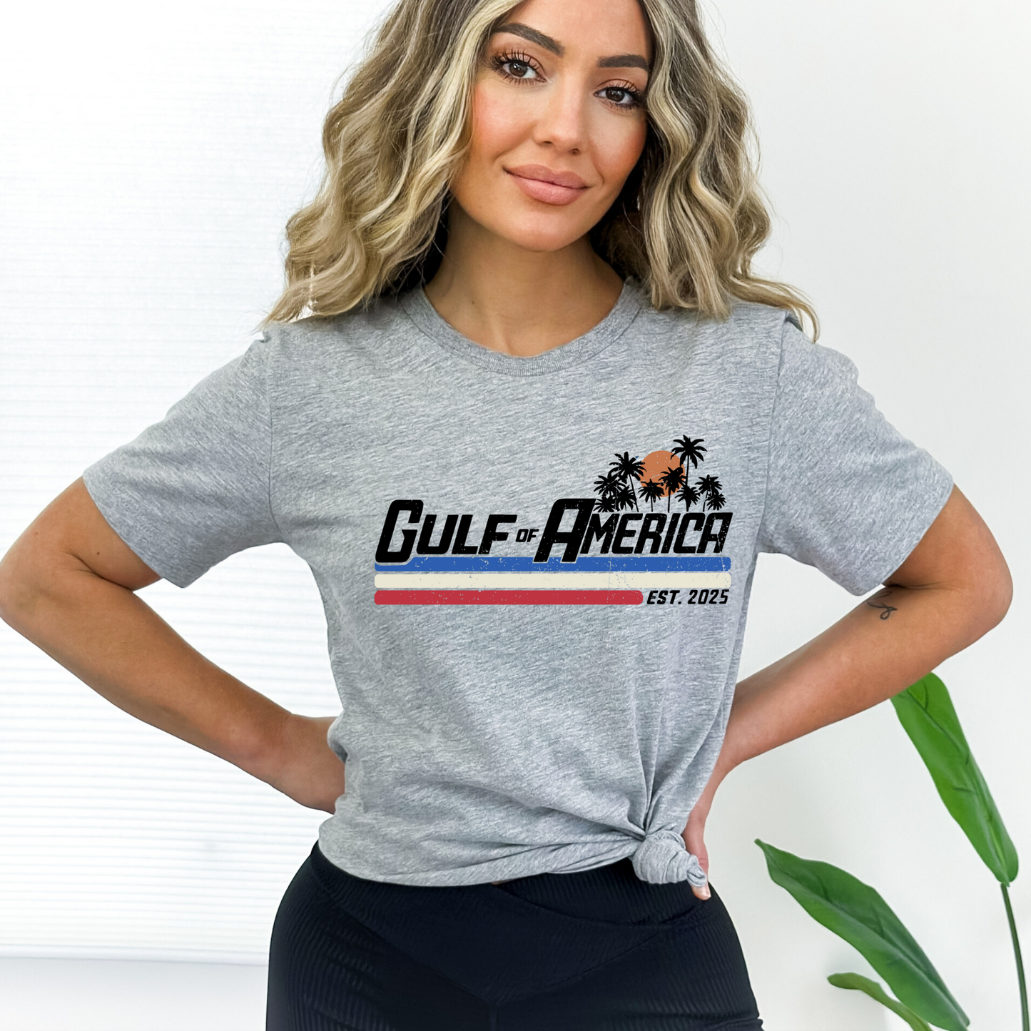 Sports gray tee with Gulf of America logo, sunset and palm trees worn casually by woman