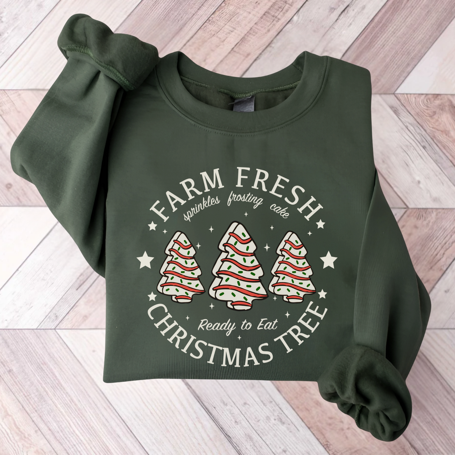 Green sweatshirt folded with “Farm Fresh Christmas Tree” design featuring frosted tree cakes