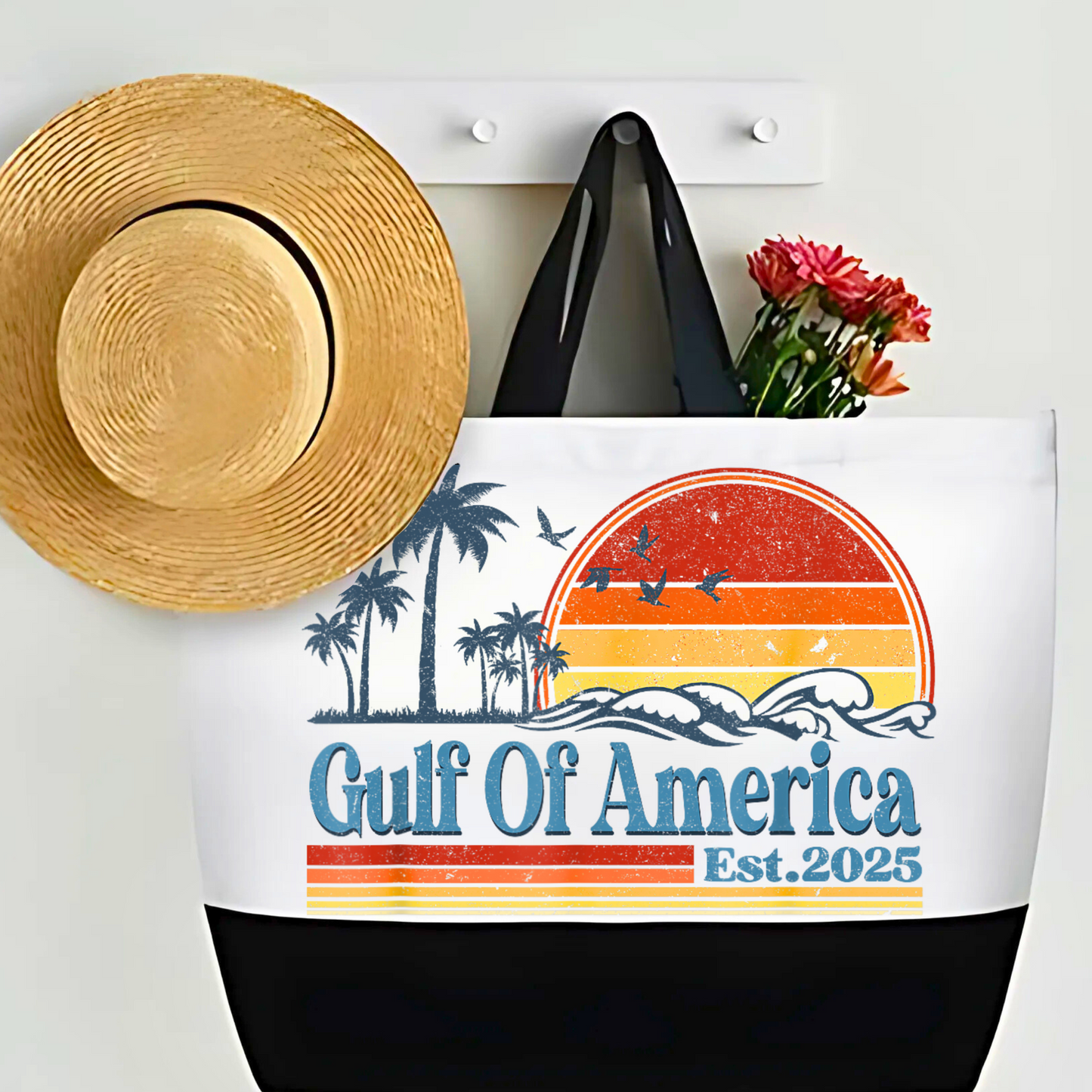 Gulf of America beach tote bag with retro sunset design and palm trees, styled on wall hook with sun hat and flowers