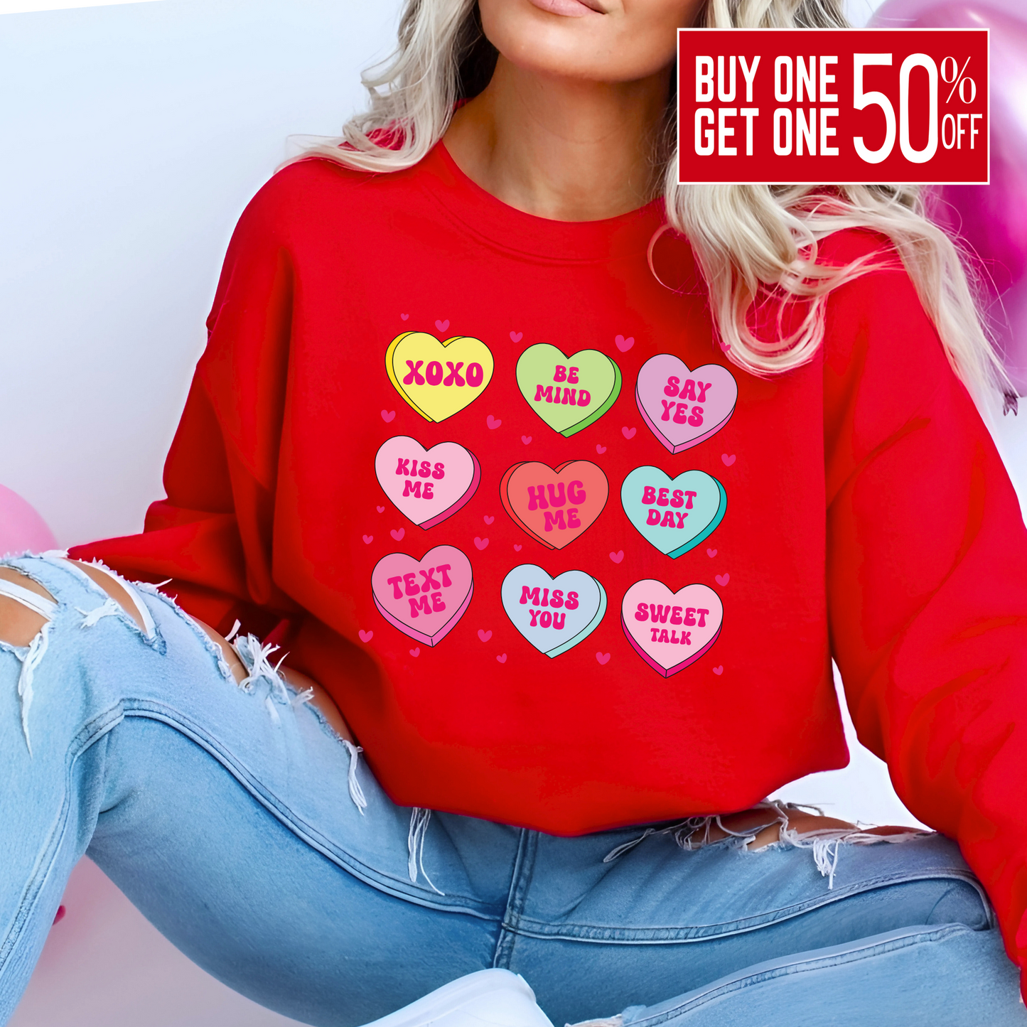 Woman wearing a red Valentine’s sweatshirt featuring colorful candy conversation hearts with messages like “XOXO,” “Be Mine,” “Say Yes,” “Kiss Me,” “Hug Me,” and more.