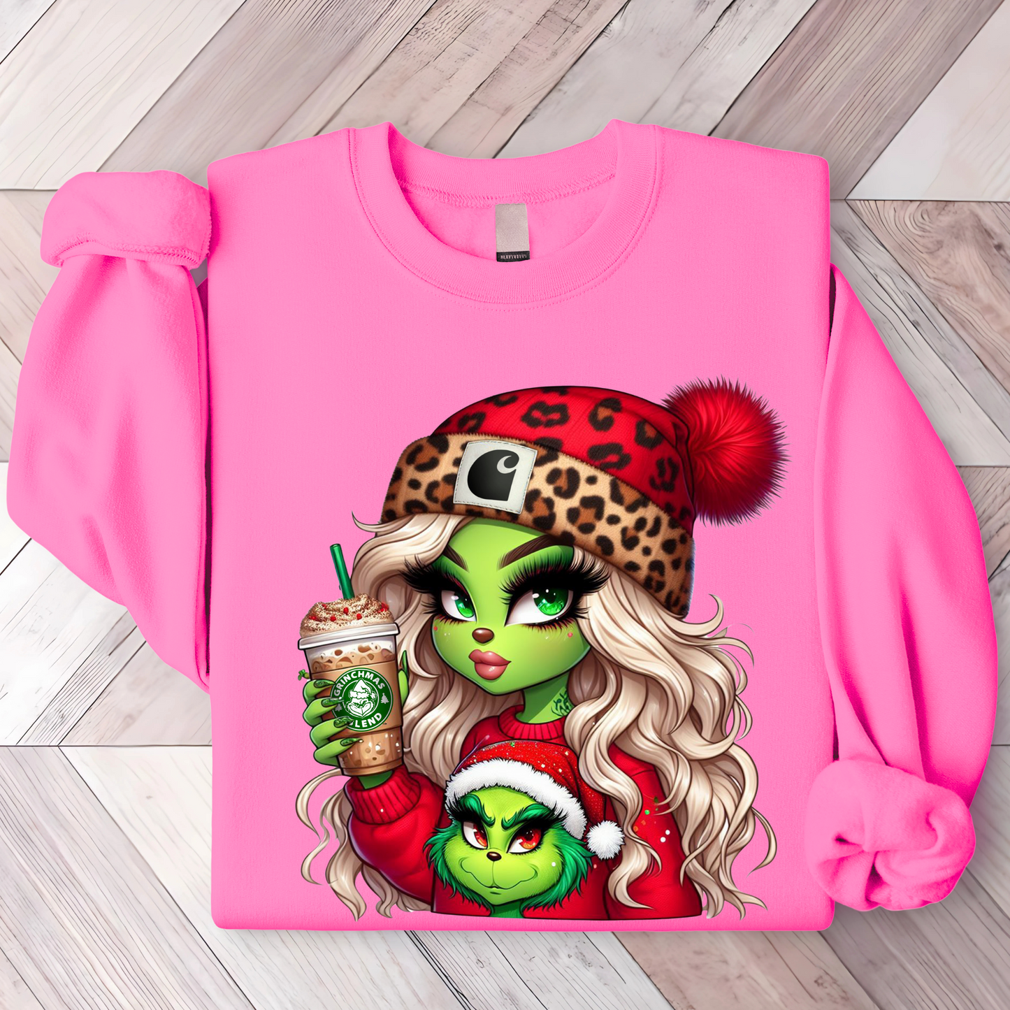 Bright pink sweatshirt with cute cartoon design of a green-skinned girl in a red sweater and animal print Santa hat holding a drink.