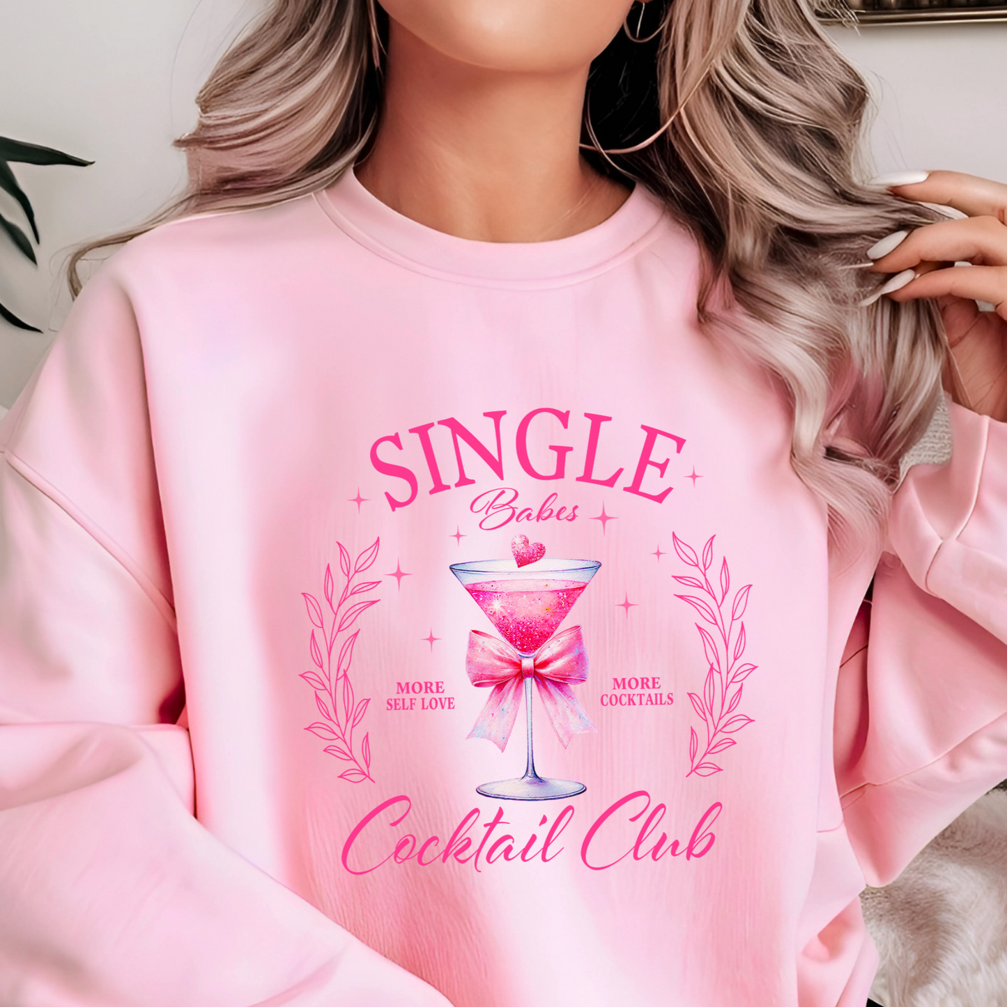 A woman wearing a pink sweatshirt with the text 'SINGLE Babes Cocktail Club' in pink design.
