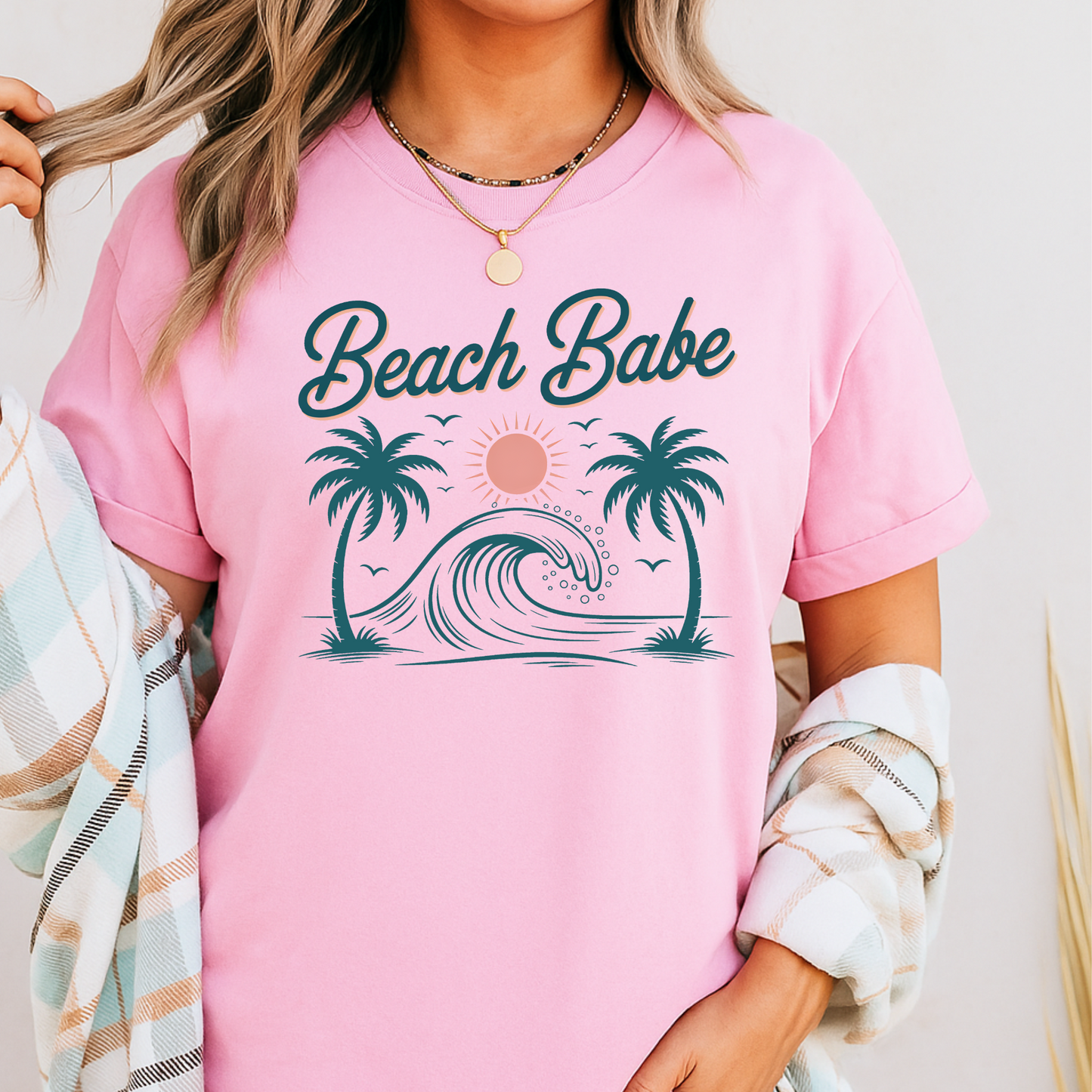 Light pink Beach Babe tee layered with plaid, standing near beach dunes