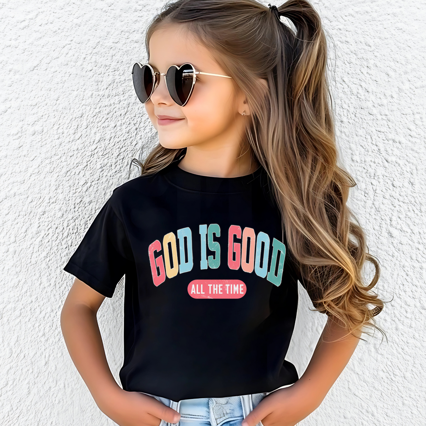Smiling girl wearing a black T-shirt with the message 'God Is Good All the Time' in colorful text, symbolizing faith and positivity. Perfect for Easter and Christian-themed apparel.