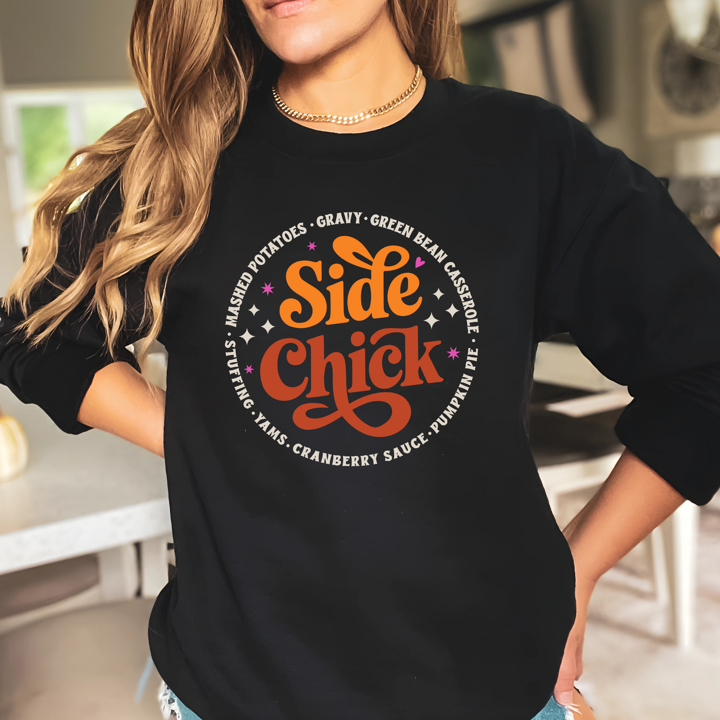 Black “Side Chick” Thanksgiving sweatshirt worn by woman in a kitchen setting. Retro text pullover perfect for hosting, holiday cooking, and fall fashion. Great Friendsgiving top or foodie gift with funny side dish theme.