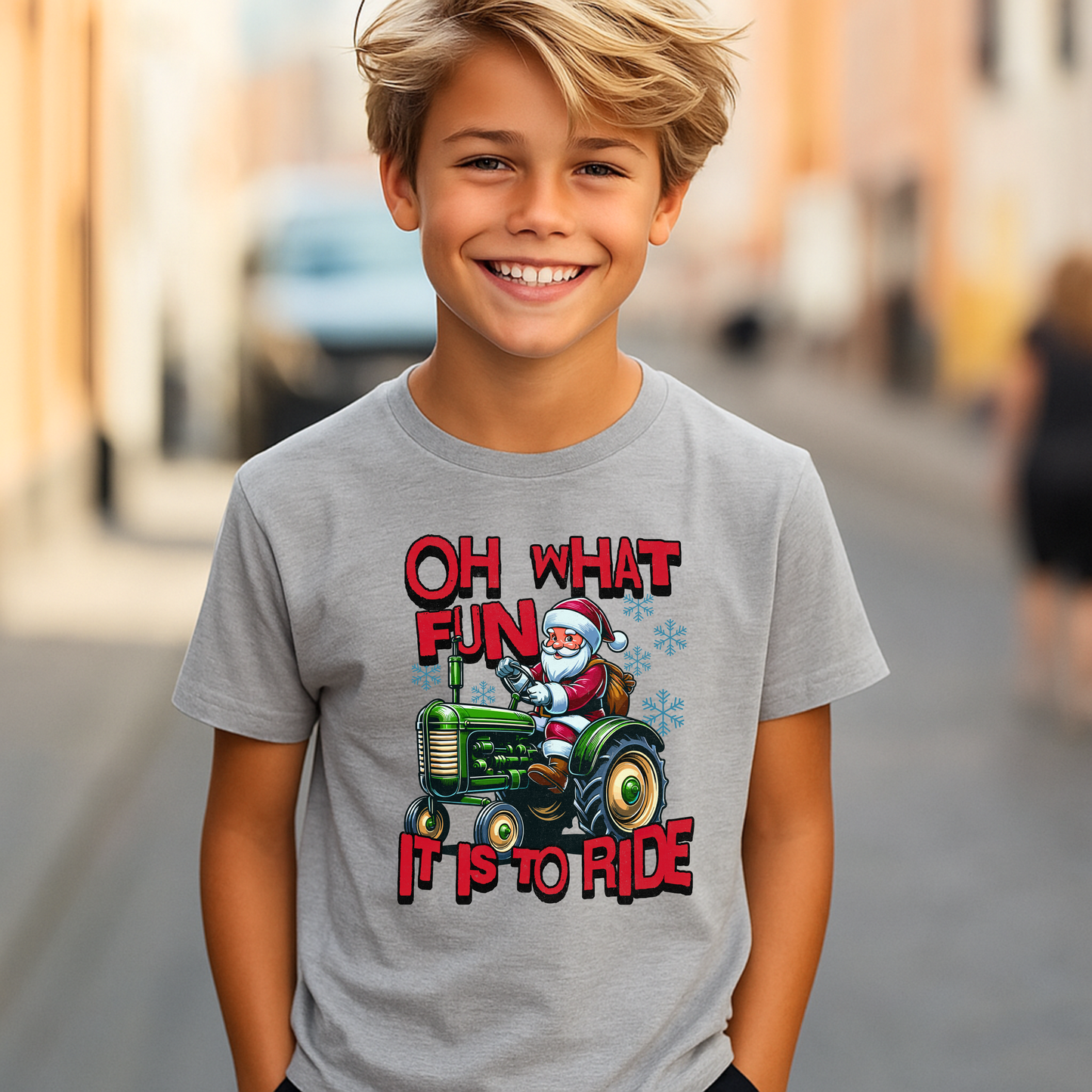 Boy modeling a gray Christmas tractor shirt featuring Santa Claus riding a green tractor with festive holiday text