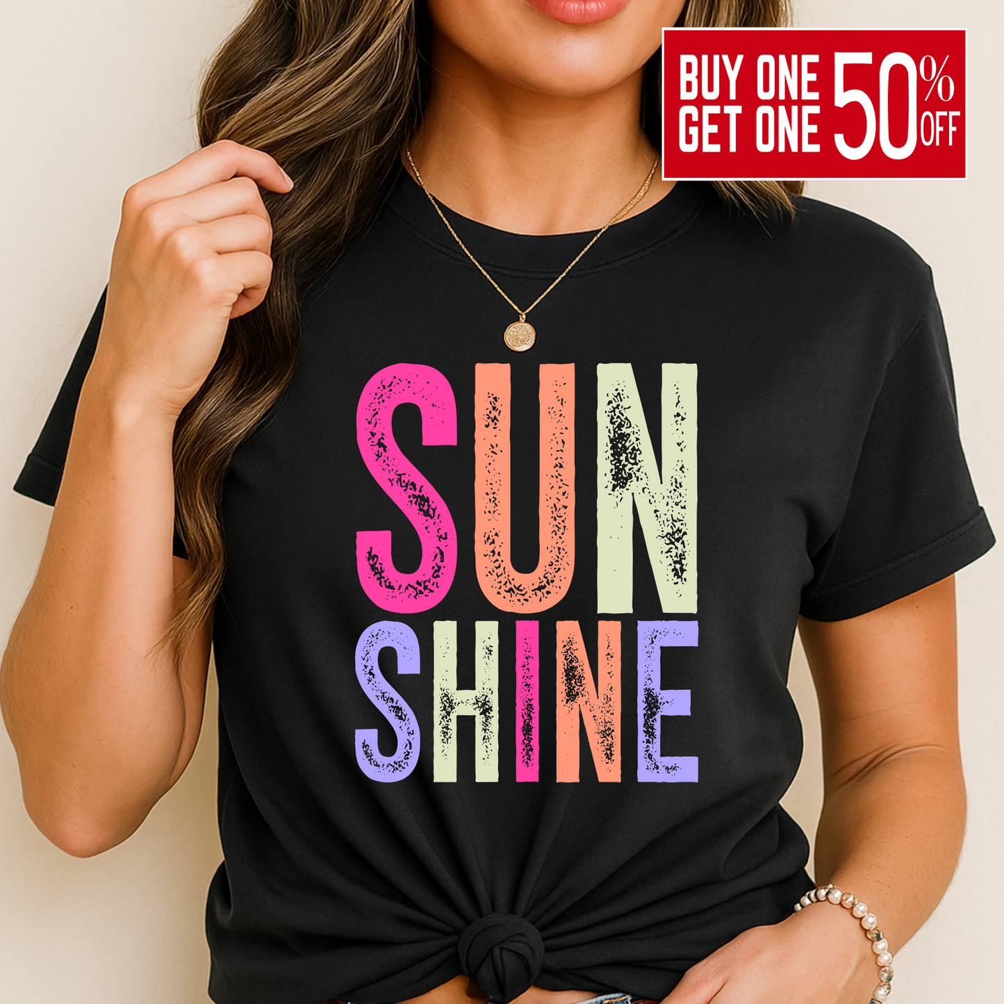 Woman wearing a bright “SUNSHINE” graphic T-shirt in Black, smiling in a relaxed summer setting.