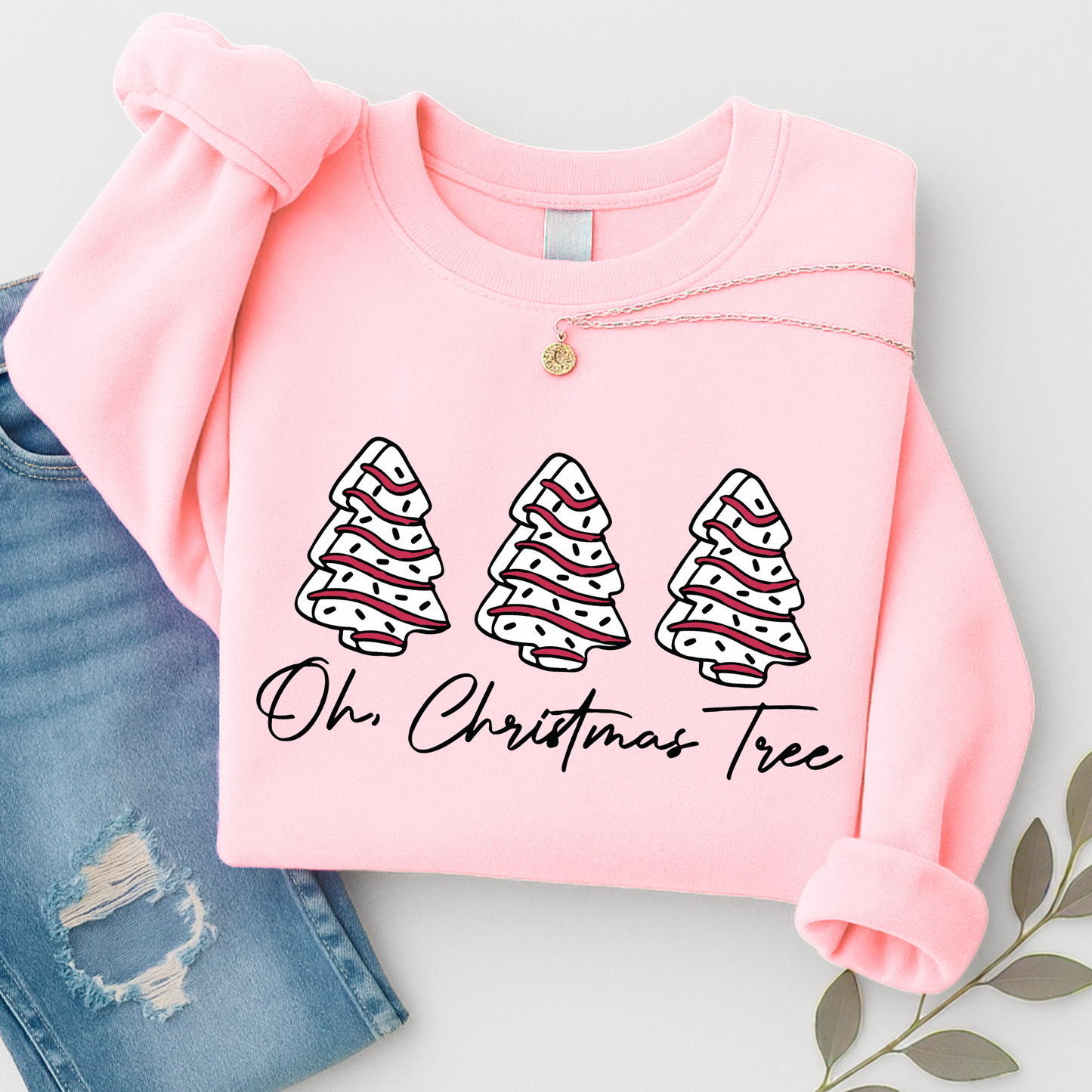 Flat lay of a Pink Christmas sweatshirt featuring three festive red and white trees with “Oh Christmas Tree” text. Styled with ripped denim and silver necklace.