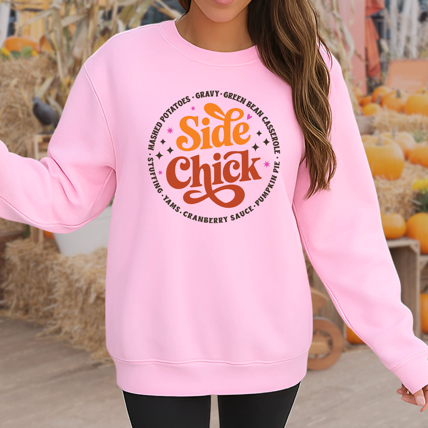 Cute light pink “Side Chick” sweatshirt worn outdoors in a fall-themed setting with pumpkins. Funny Thanksgiving pullover for women, perfect for Friendsgiving, autumn vibes, and cozy fall outfits. Unisex retro holiday sweater featuring side dish favorites.