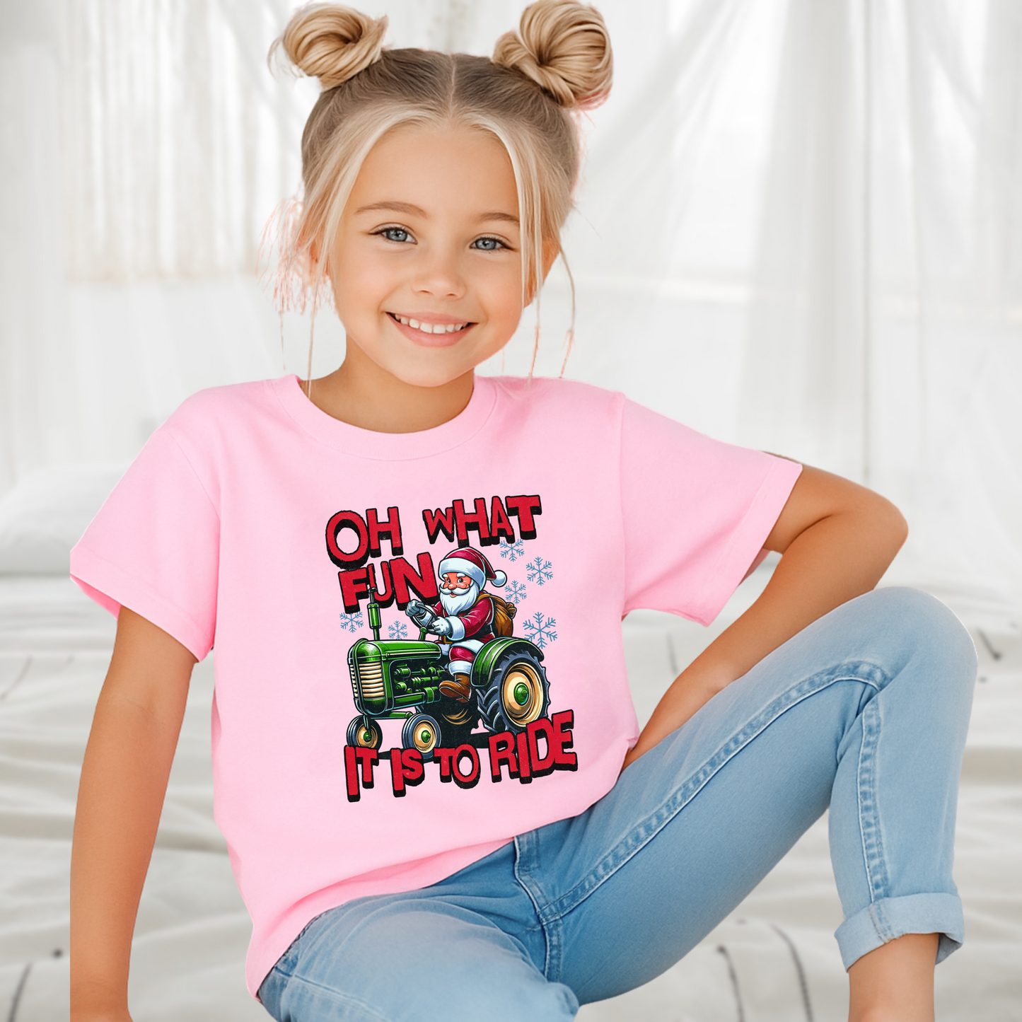 Girl sitting indoors in a pink youth Christmas shirt showing Santa riding a tractor with festive holiday design.