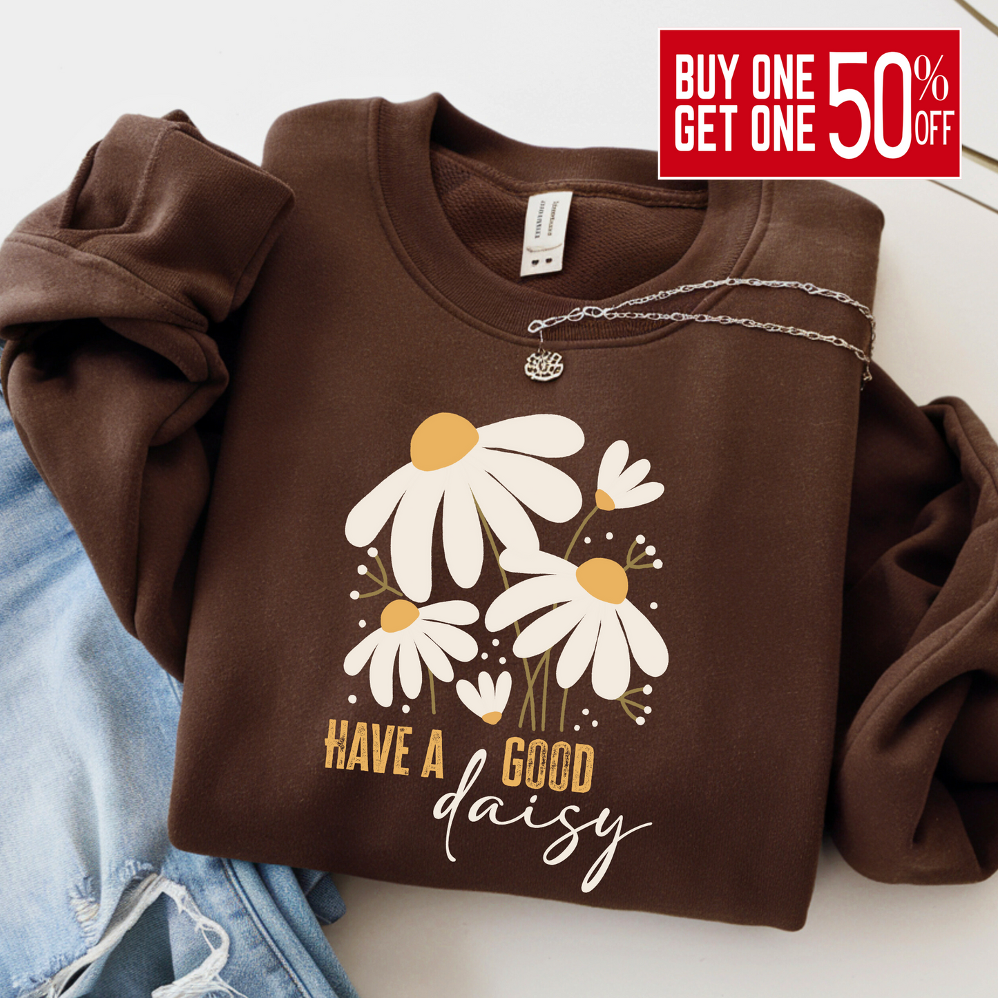 Chocolate brown “Have a Good Daisy” sweatshirt folded with jeans and a necklace, featuring a cozy fall floral graphic perfect for seasonal outfits, pumpkin patch days, or casual autumn layering.