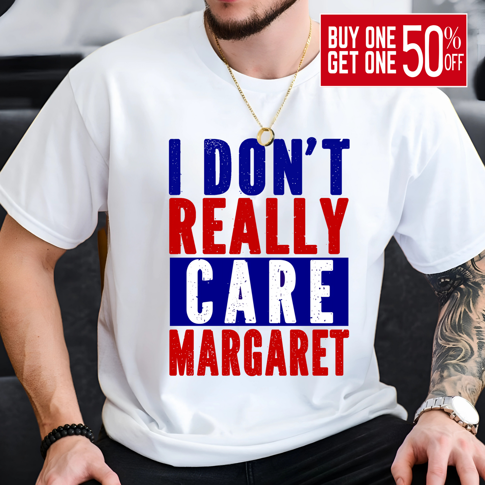 Man sitting and wearing a white patriotic graphic tee with red, white, and blue block lettering that says "I Don’t Really Care Margaret"