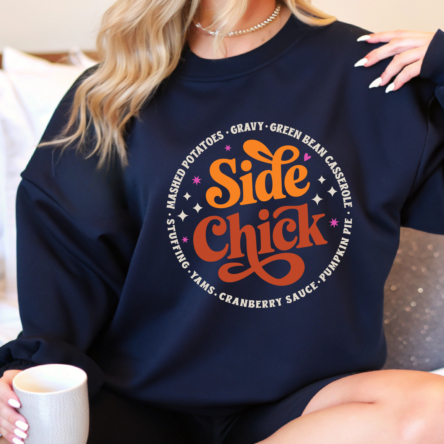 Navy blue “Side Chick” sweatshirt styled indoors with cozy fall vibes. Funny Thanksgiving pullover for lounging, holiday photos, or gifting. Features festive side dish design with retro colors and soft unisex fit.