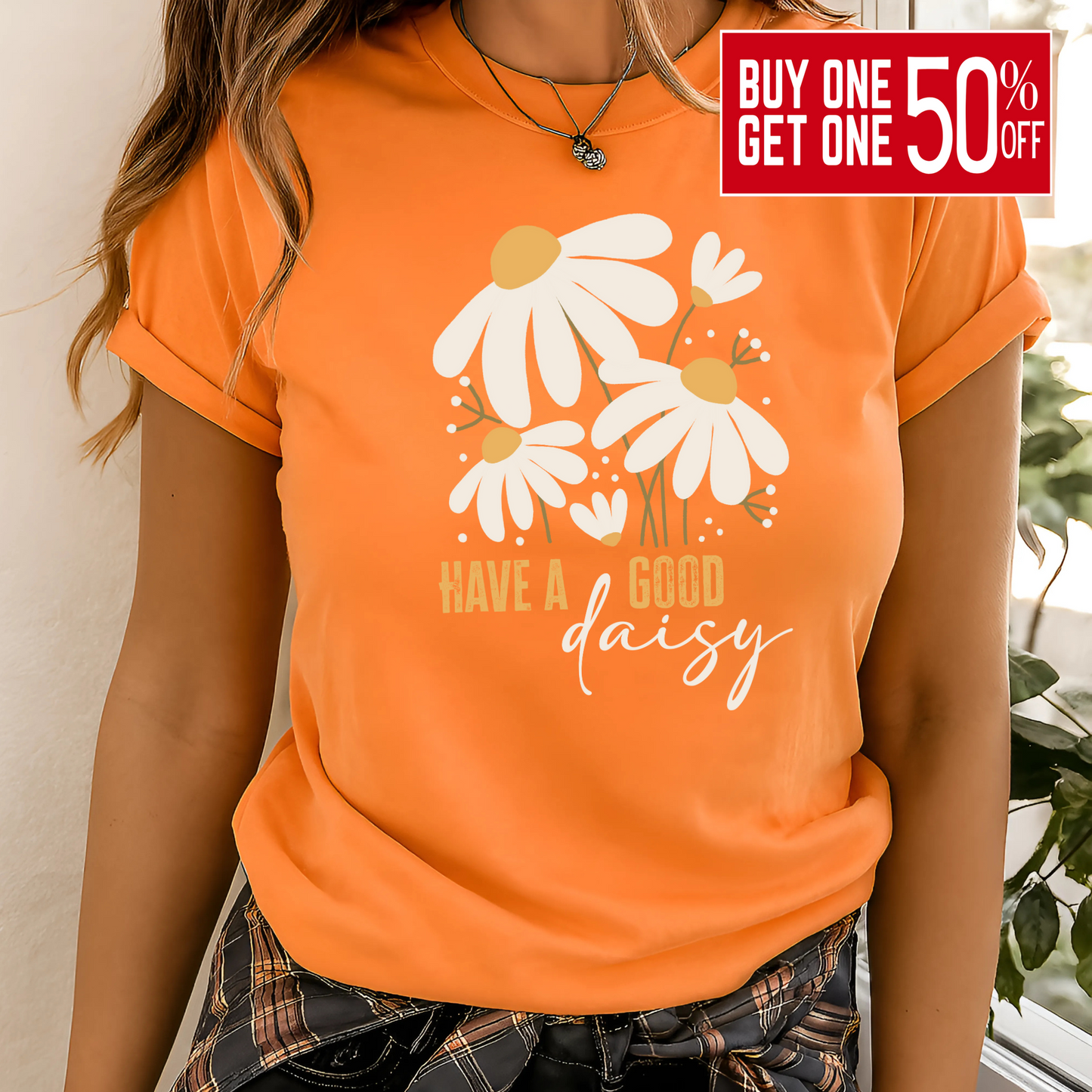 Orange “Have a Good Daisy” T-shirt with white daisy graphic and retro lettering, styled for fall with warm tones and seasonal outfit layering.