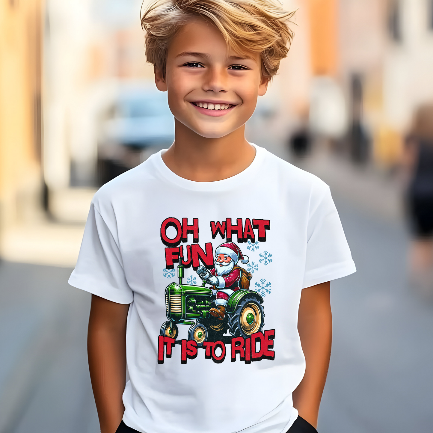 Smiling boy wearing a white youth unisex Christmas T-shirt with Santa Claus driving a green tractor and the words “Oh What Fun It Is to Ride.”,