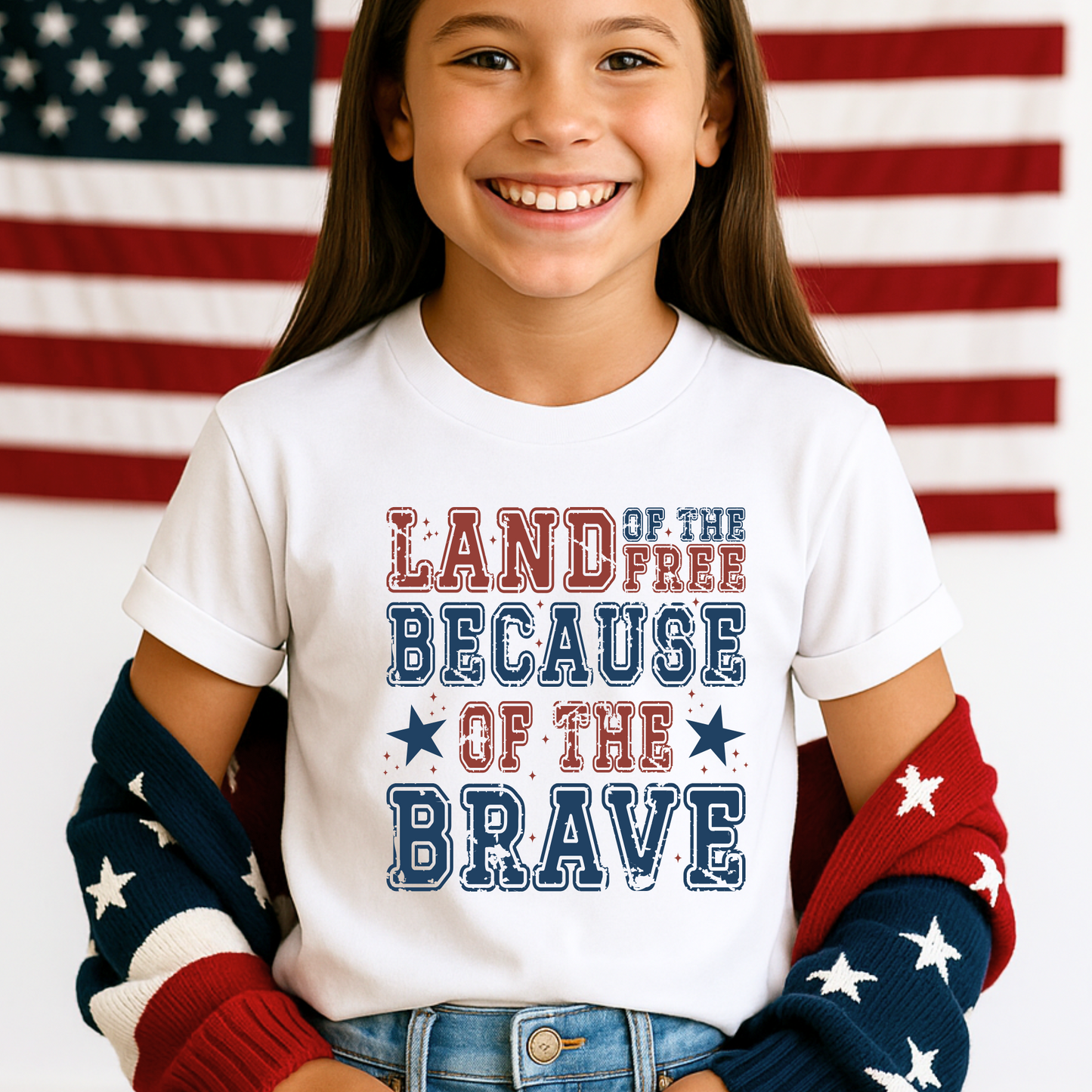 Tween girl smiling in a white "Land of the Free Because of the Brave" shirt with rolled sleeves and red-white-blue cardigan.