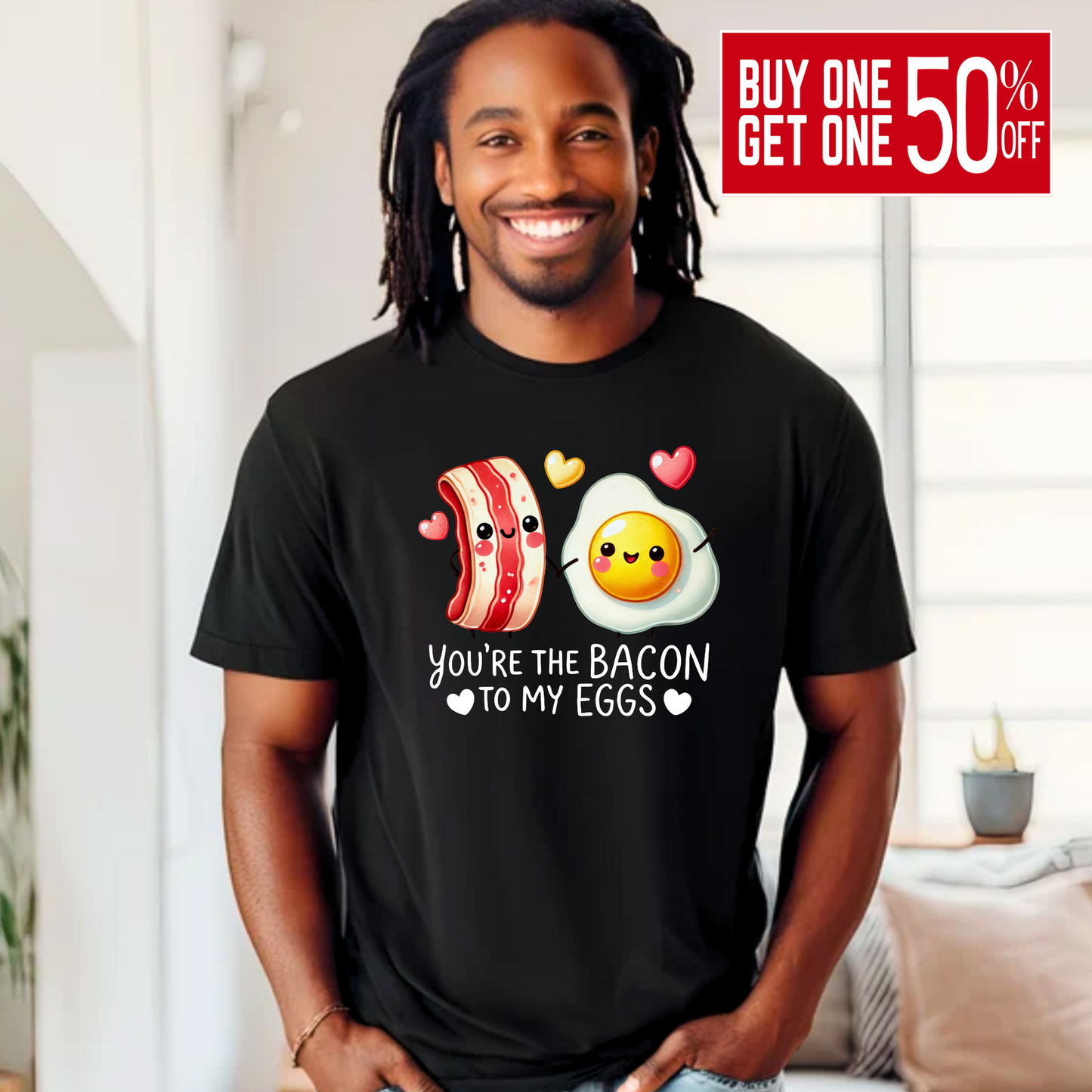 Smiling man wearing a black T-shirt with kawaii-style bacon and egg holding hands, surrounded by colorful hearts. Design says 'You're the bacon to my eggs