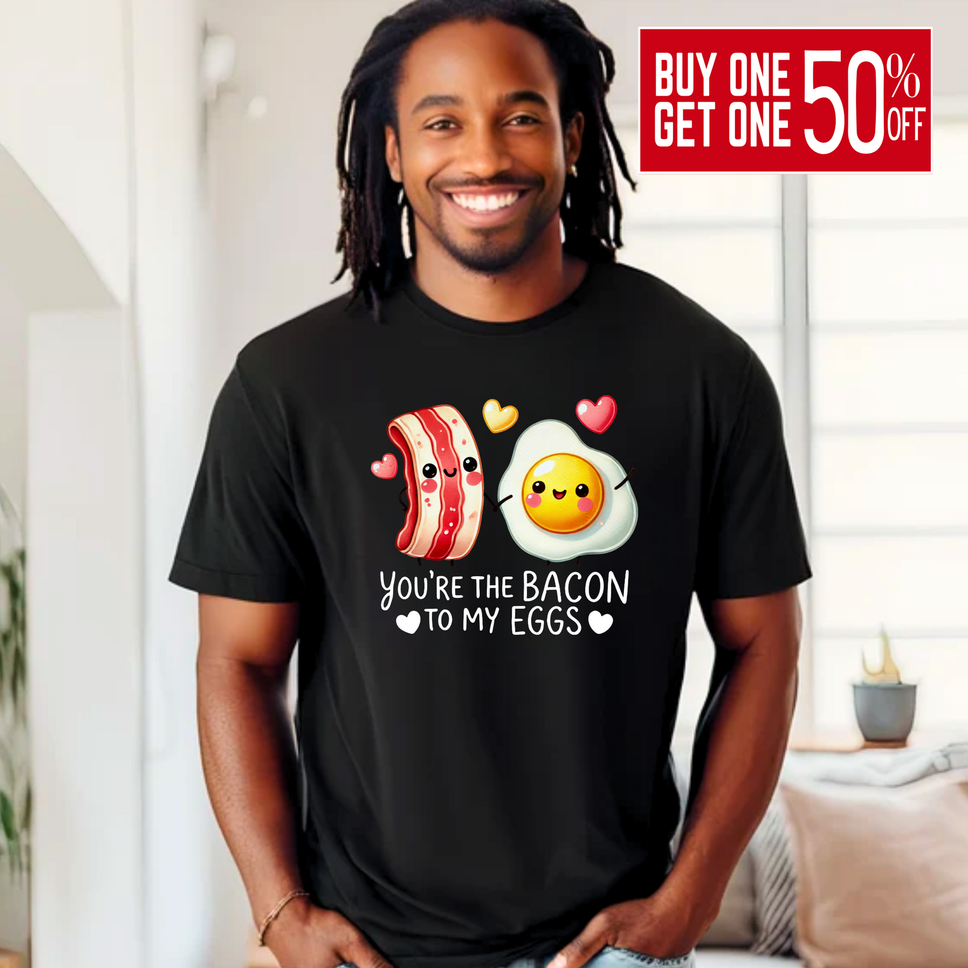 Smiling man wearing a black T-shirt with kawaii-style bacon and egg holding hands, surrounded by colorful hearts. Design says 'You're the bacon to my eggs