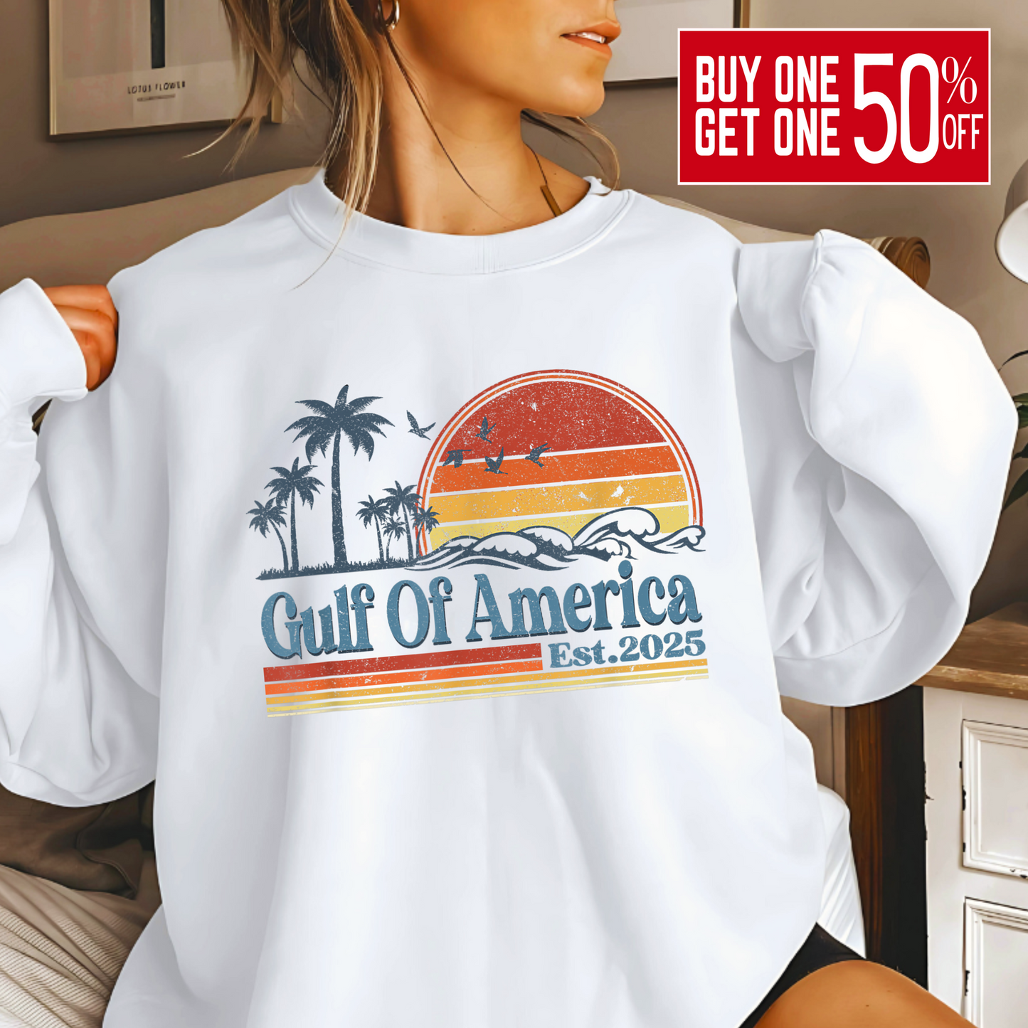 Woman wearing a white Gulf of America Est. 2025 sweatshirt featuring vintage sunset, palm trees, and ocean wave graphic in red, orange, and yellow tones