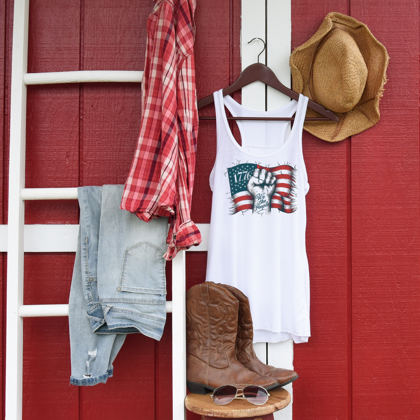 White tank top with patriotic design hanging on ladder with jeans and hat