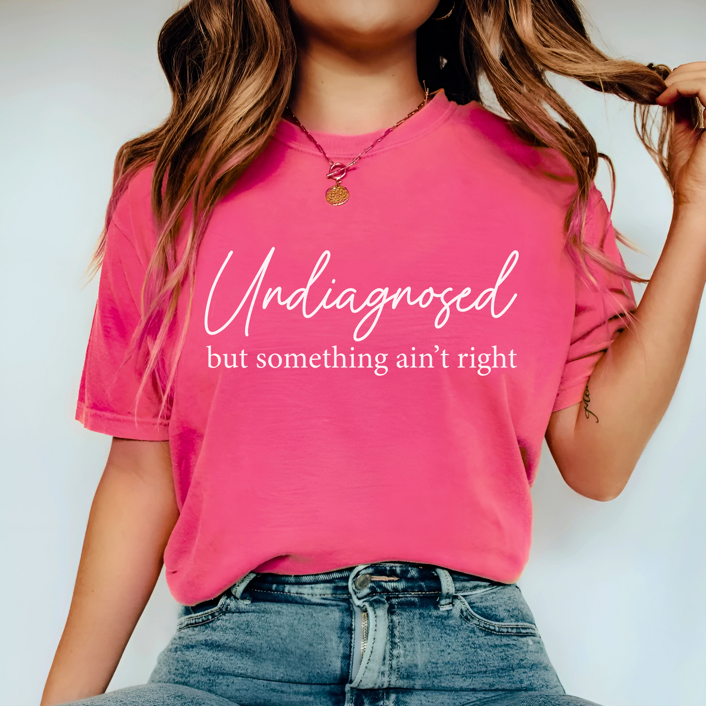 Woman in pink shirt with “Undiagnosed but something ain’t right” in white script