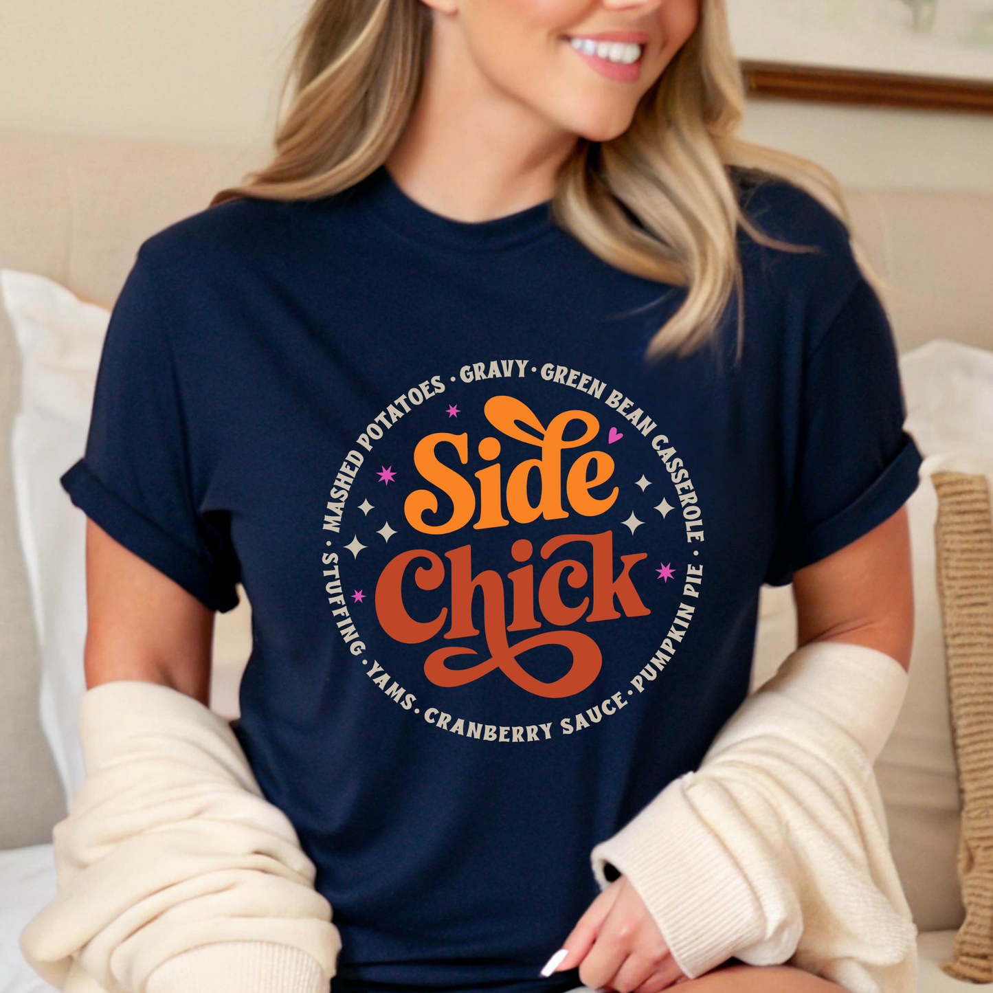 Woman seated on a bed in a navy “Side Chick” tee with cozy cardigan. Retro-style graphic surrounded by Thanksgiving side dishes. A perfect fall shirt for relaxing, baking, or hosting. Great for women looking for comfy, casual, and cute autumn outfit ideas for Friendsgiving or family dinner.