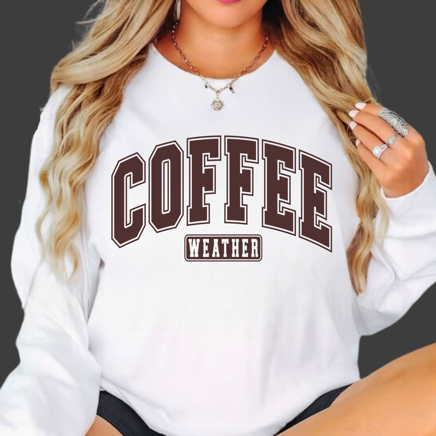 Woman wearing white crewneck sweatshirt with bold brown “Coffee Weather” text