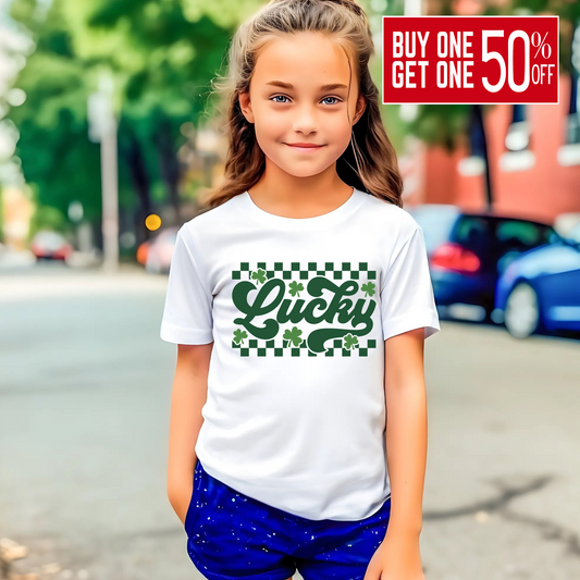 White T-shirt with 'Lucky' in green cursive, surrounded by shamrocks and a checkered pattern – perfect for St. Patrick’s Day.