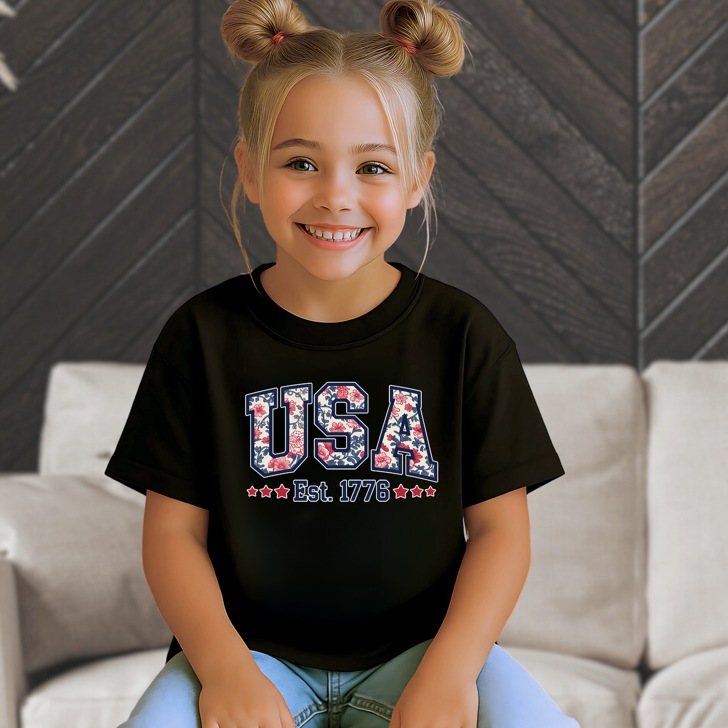 Youth girl smiling in a black USA Est. 1776 t-shirt, seated indoors.