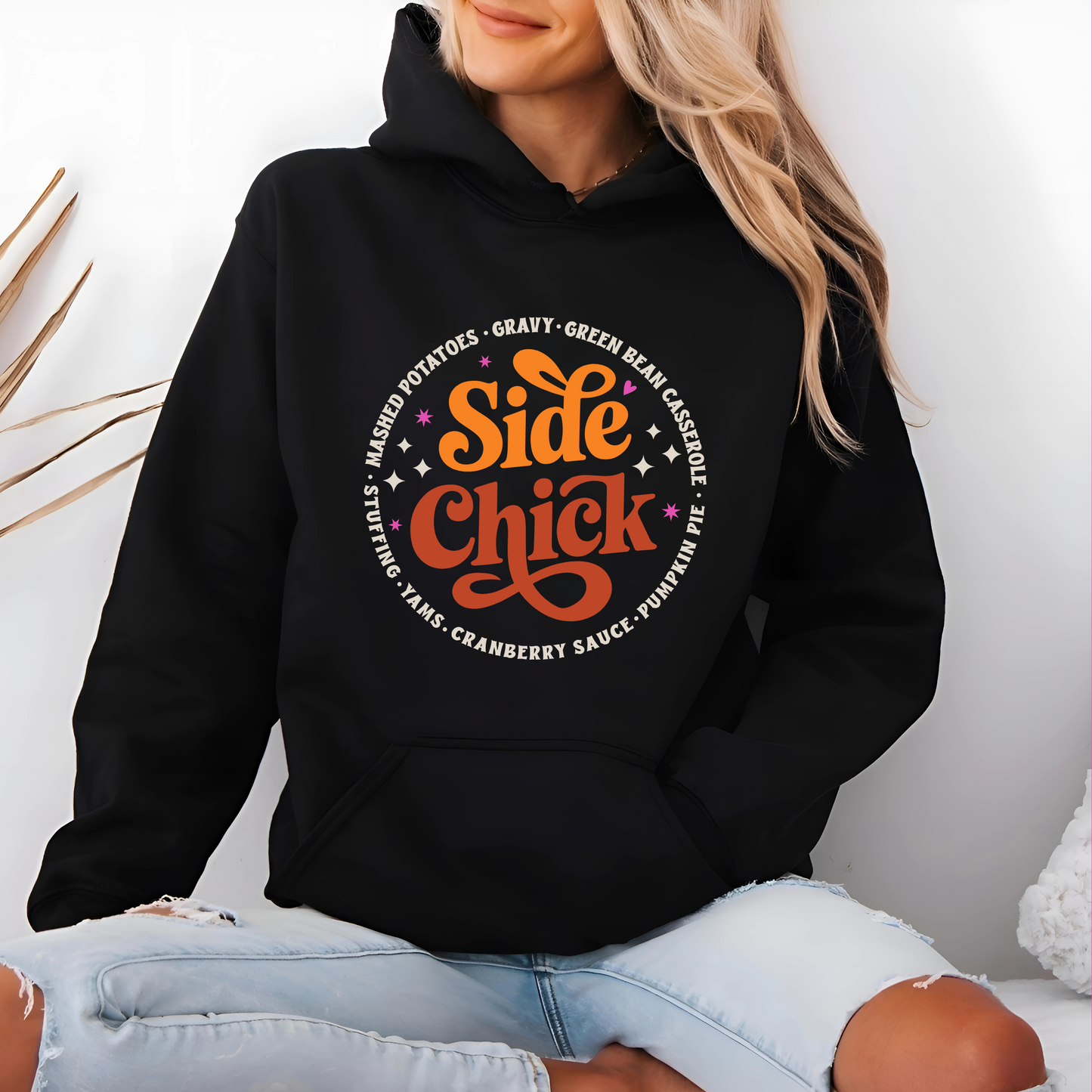 Woman sitting in a black “Side Chick” hoodie with festive Thanksgiving graphic design. Soft, warm, and perfect for holiday lounging or family dinner. Great for celebrating fall in style.