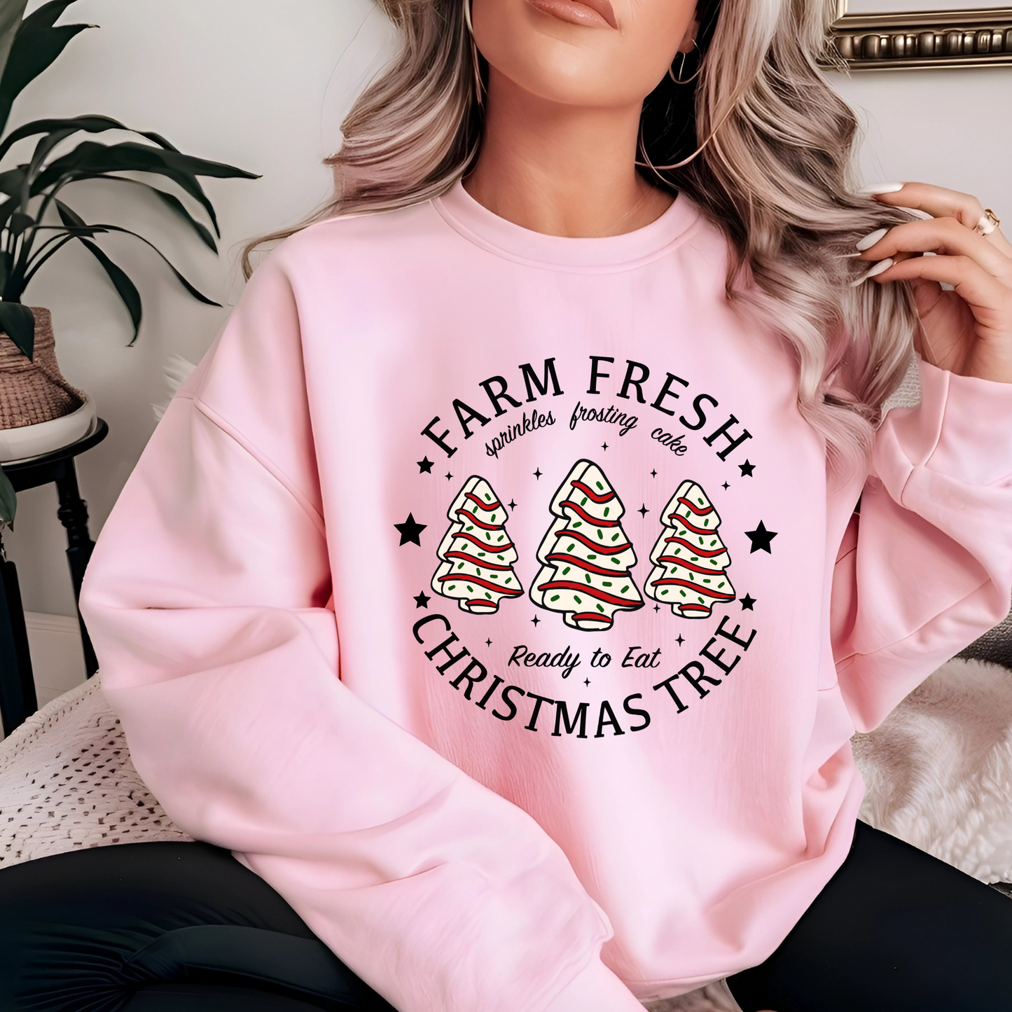 Woman in pink Christmas sweatshirt with frosted tree cakes by a Christmas tree