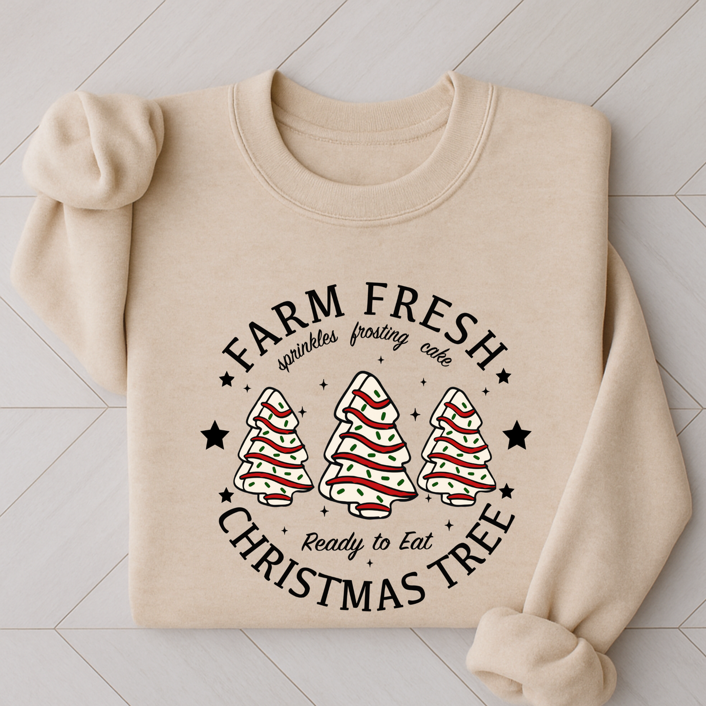 Sand colored sweatshirt folded with “Farm Fresh Christmas Tree” design featuring frosted tree cakes