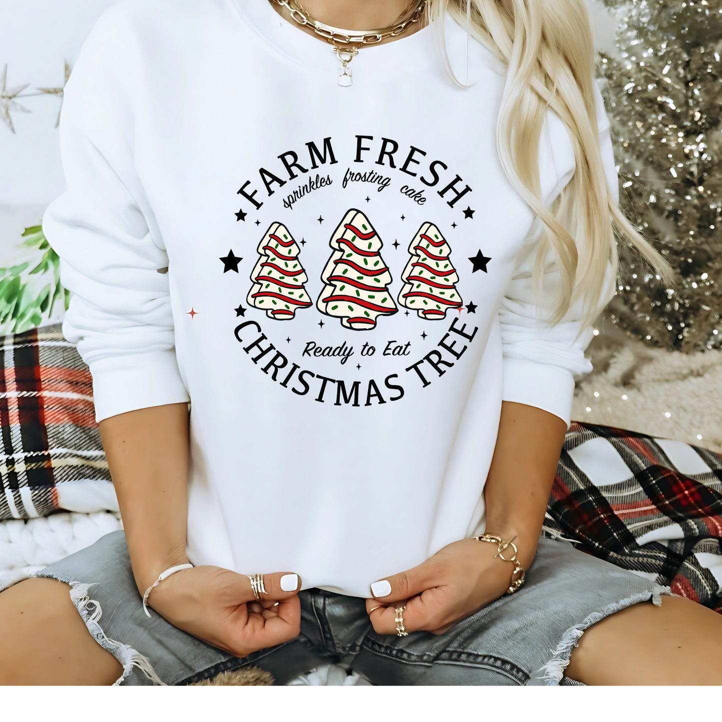 Woman in white Christmas sweatshirt with frosted tree cakes by a Christmas tree