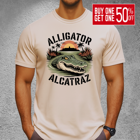 Athletic man wearing a sand-colored Alligator Alcatraz T-shirt. Graphic includes an aggressive alligator in marsh water with a distant sunset over Alcatraz. Perfect rugged men’s shirt for outdoor lovers and vacation style.

