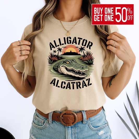 Woman in a beige Alligator Alcatraz T-shirt with vivid gator and sunset design. Soft unisex cotton tee styled with denim, great for travel or casual days.