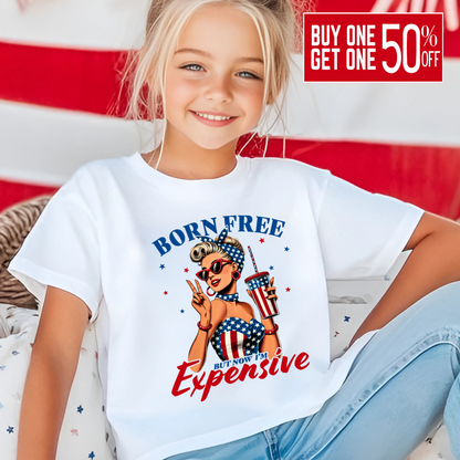Child wearing a white t-shirt with 'Born Free But Now It's Expensive' graphic design in front of an American flag.