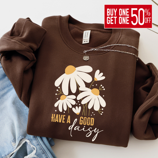 Chocolate brown “Have a Good Daisy” sweatshirt folded with jeans and a necklace, featuring a cozy fall floral graphic perfect for seasonal outfits, pumpkin patch days, or casual autumn layering.
