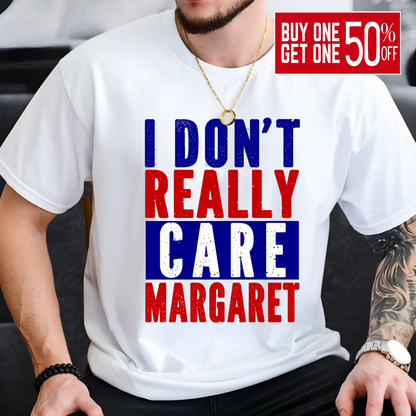 Man sitting and wearing a white patriotic graphic tee with red, white, and blue block lettering that says "I Don’t Really Care Margaret"