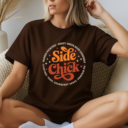 Model lounging in a dark brown “Side Chick” graphic tee, surrounded by cozy neutral fall décor. Features vintage-inspired Thanksgiving design perfect for November, autumn gatherings, or staying comfy on turkey day. Cute Friendsgiving outfit idea or gift for your foodie bestie.