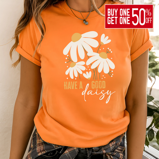 Orange “Have a Good Daisy” T-shirt with white daisy graphic and retro lettering, styled for fall with warm tones and seasonal outfit layering.