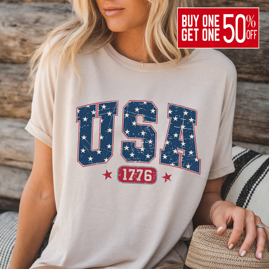 USA 1776 graphic T-shirt in sand color, patriotic tee styled for summer by woman sitting on wooden bench