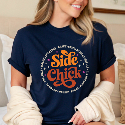 Woman seated on a bed in a navy “Side Chick” tee with cozy cardigan. Retro-style graphic surrounded by Thanksgiving side dishes. A perfect fall shirt for relaxing, baking, or hosting. Great for women looking for comfy, casual, and cute autumn outfit ideas for Friendsgiving or family dinner.