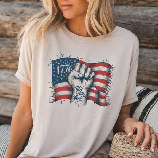 Woman sitting in neutral 1776 shirt outdoors with rustic wood background.

