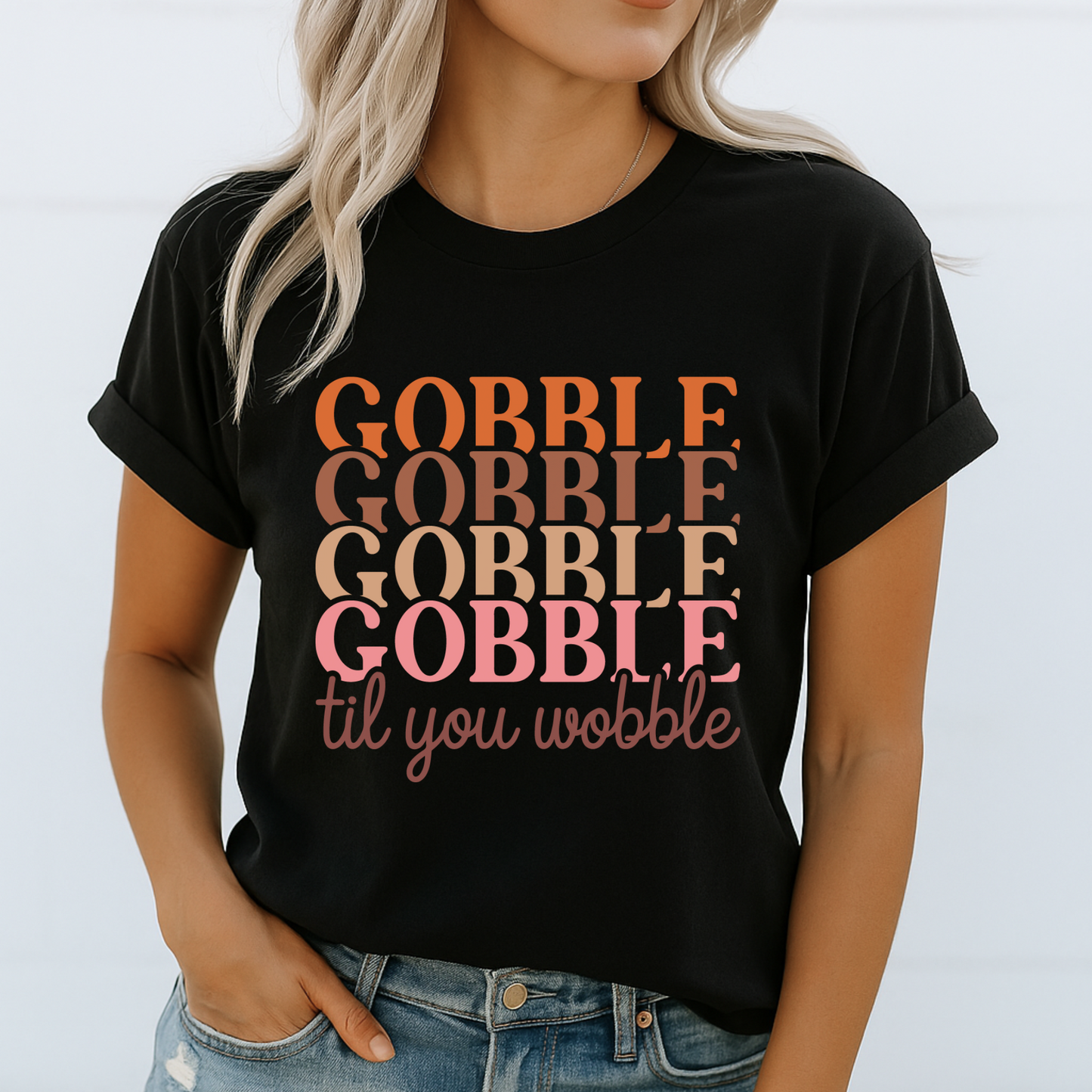 Woman wearing a black “Gobble Til You Wobble” shirt with retro text, styled casually with rolled sleeves and jeans – perfect fall Thanksgiving outfit
