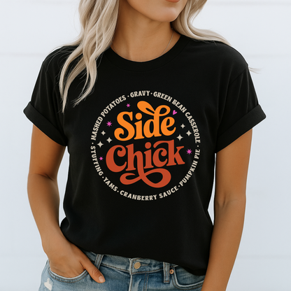 Woman wearing a black “Side Chick” shirt with orange and brown Thanksgiving graphic. Rolled sleeve detail and light-wash jeans create a casual fall look. Bold seasonal design for stuffing and gravy lovers. Ideal for women, teens, and moms who want comfy and funny turkey day fashion.