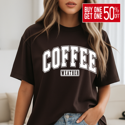 Woman wearing brown "Coffee Weather" shirt standing by bed, cozy fall look