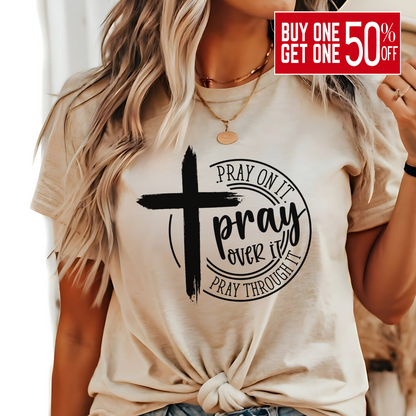 Woman wearing tan T-shirt with black cross graphic and inspirational pray wording.