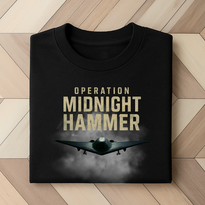 Folded black t-shirt with bold Operation Midnight Hammer design and B-2 stealth bomber emerging from smoke. Military airstrike-inspired patriotic apparel for men and women, ideal for 4th of July or Armed Forces support.