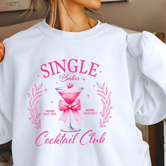 A woman sitting while wearing a white long-sleeve sweatshirt with text and a pink bow on it, indicating a playful and romantic theme appropriate for Valentine's Day.